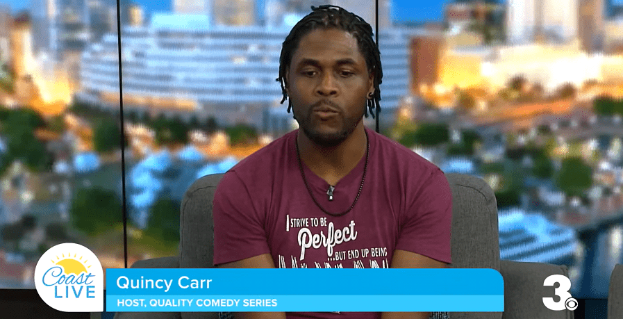 Quincy Carr, host of the Quality Comedy Series, discusses upcoming events on a talk show set with a vibrant cityscape in the background.