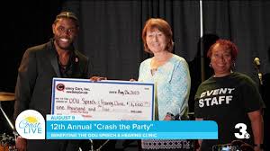 Three people hold a large check for $1,600 during the 12th Annual "Crash the Party" event, supporting a health clinic. The celebration highlights community engagement.